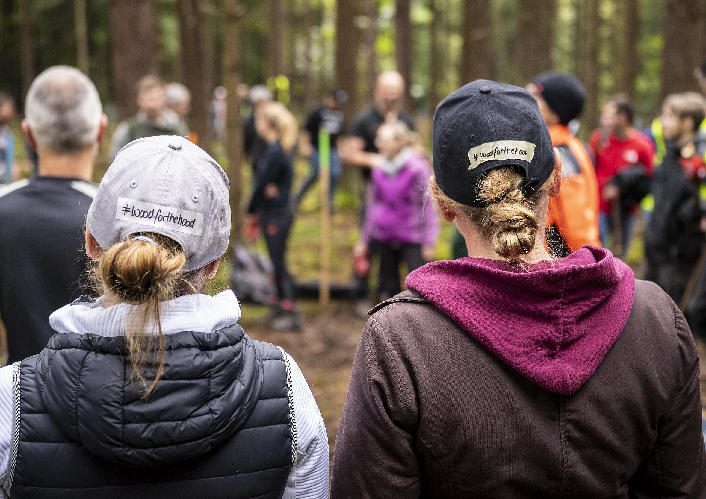 Zwei Frauen mit Schildkappen, auf deren Hinterkopf #woodforthehood steht.