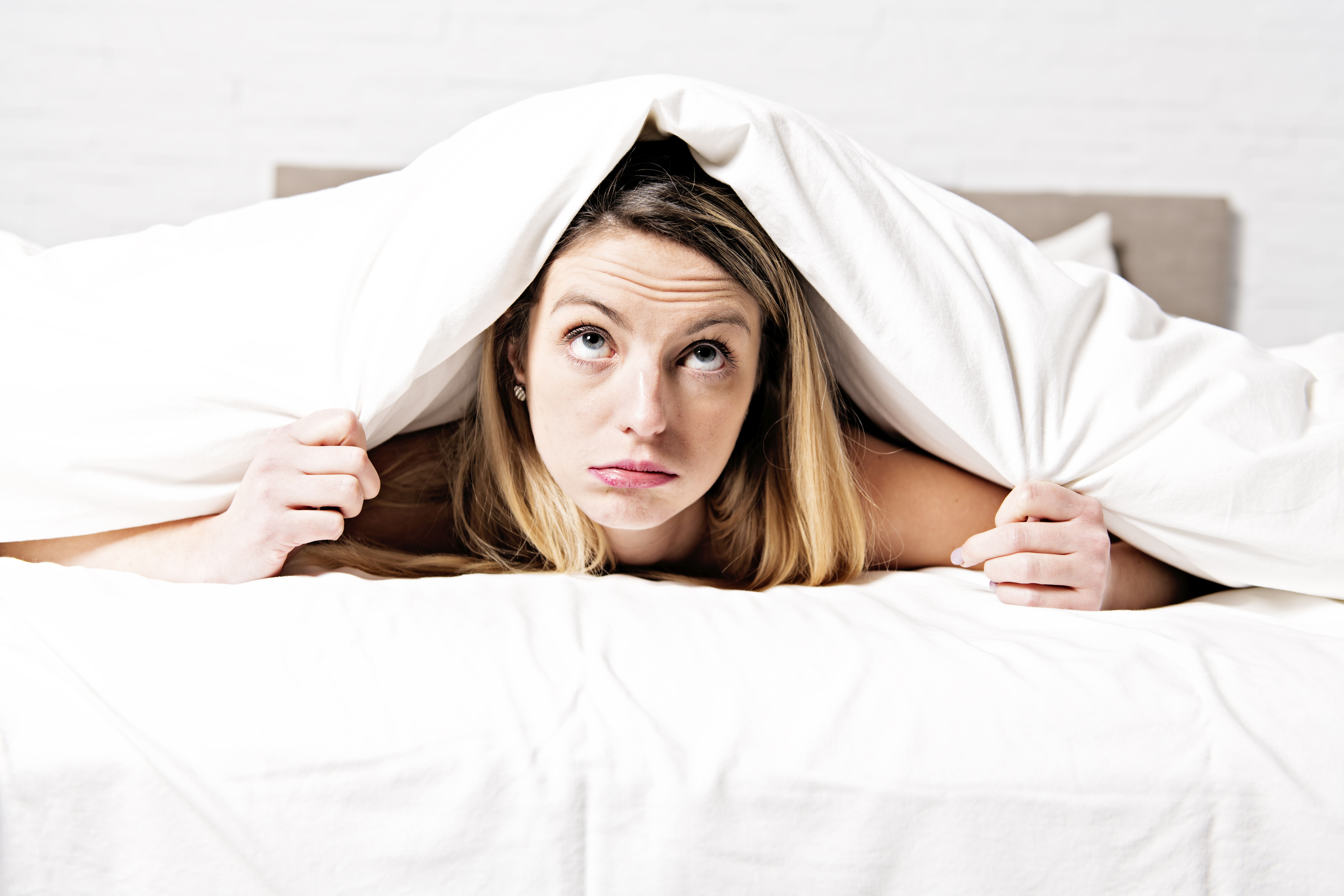 Eine nachdenkliche Frau liegt im Bett und zieht die Decke über ihren Kopf.